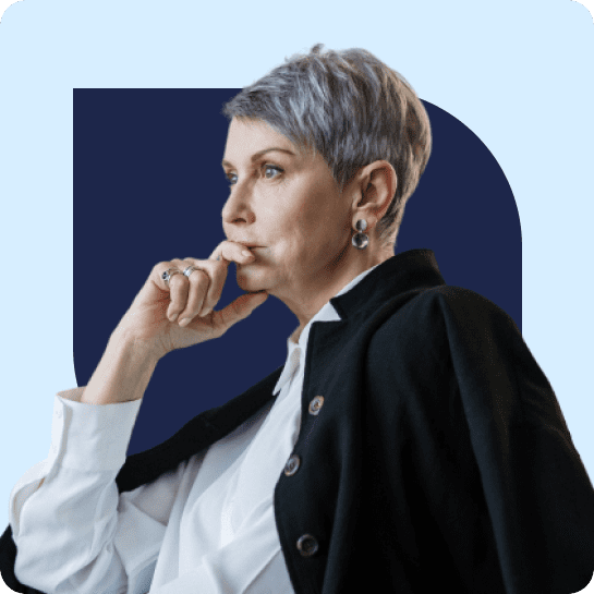 Femme mûre aux cheveux gris courts et aux boucles d'oreilles, vêtue d'un blazer noir et d'un chemisier blanc, touchant pensivement son menton.
