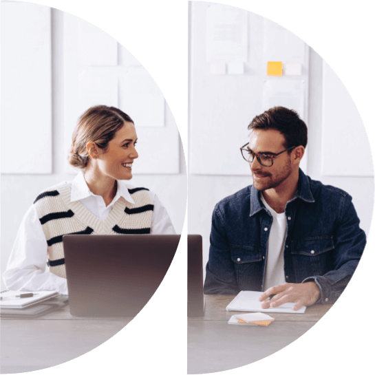 Deux professionnels dans un bureau moderne, avec une femme utilisant un ordinateur portable et un homme écrivant des notes, tous deux souriants et engagés dans une conversation.